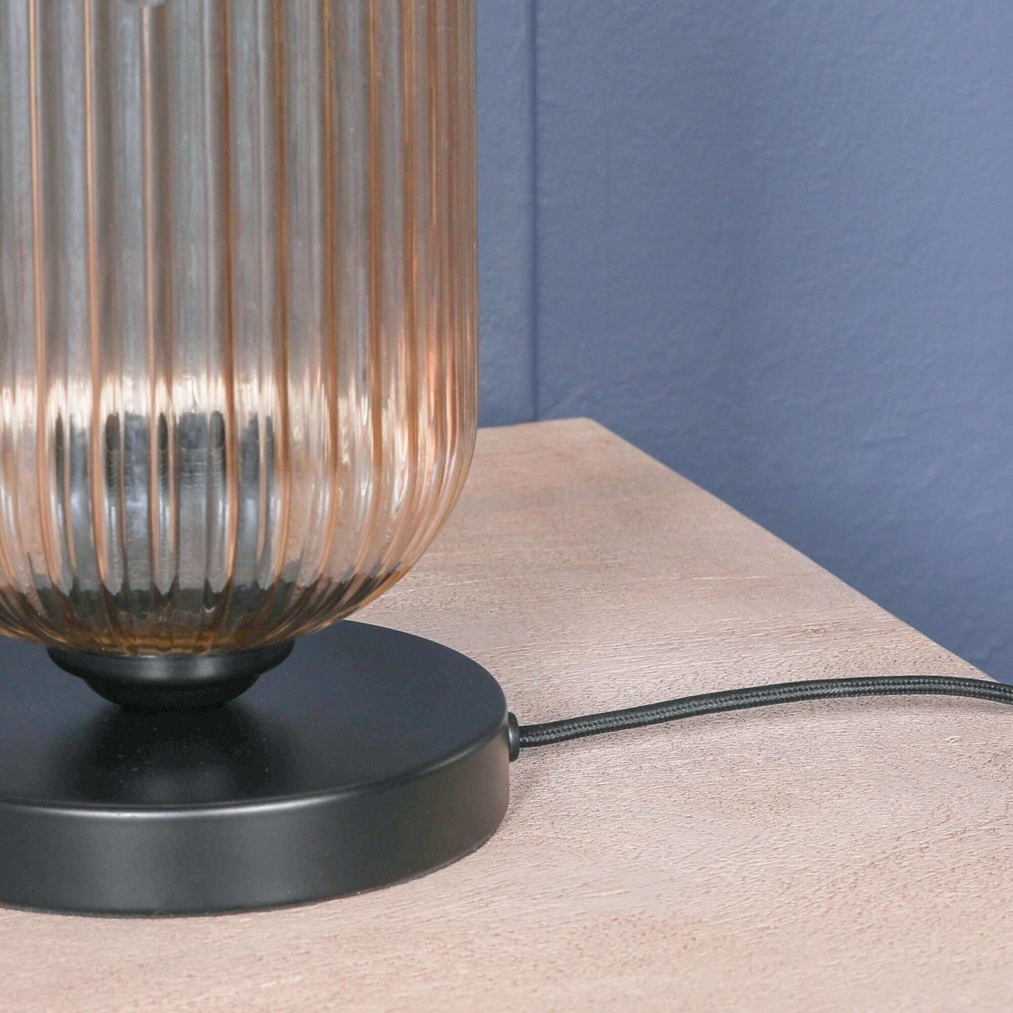 Detail of industrial black table lamp with smoked glass shade and in-line toggle switch on a wooden surface.