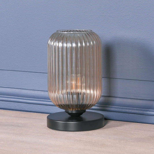 Industrial style black table lamp with smoked glass fluted shade, casting a warm glow on a simple surface.