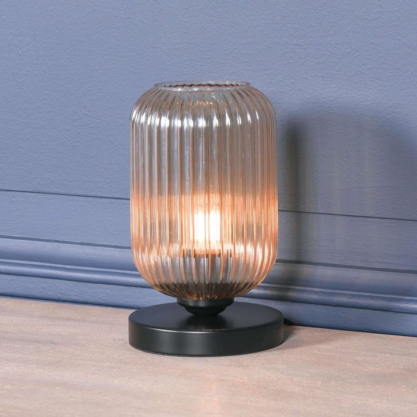 Industrial style black table lamp with smoked glass fluted shade, casting warm ambient light in a modern decor.