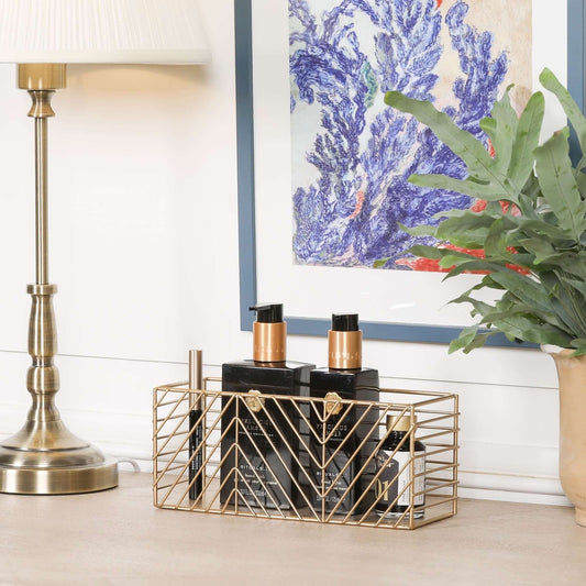Gold metal storage basket with stylish design, organising beauty products on a desk.