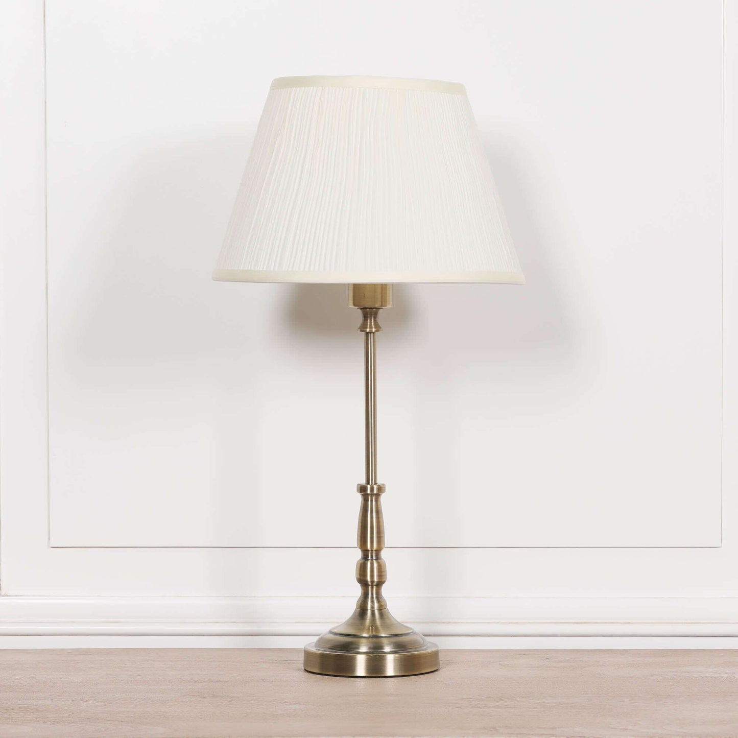 Traditional satin brass candlestick lamp with cream pleated shade, offering elegance and warm ambiance.