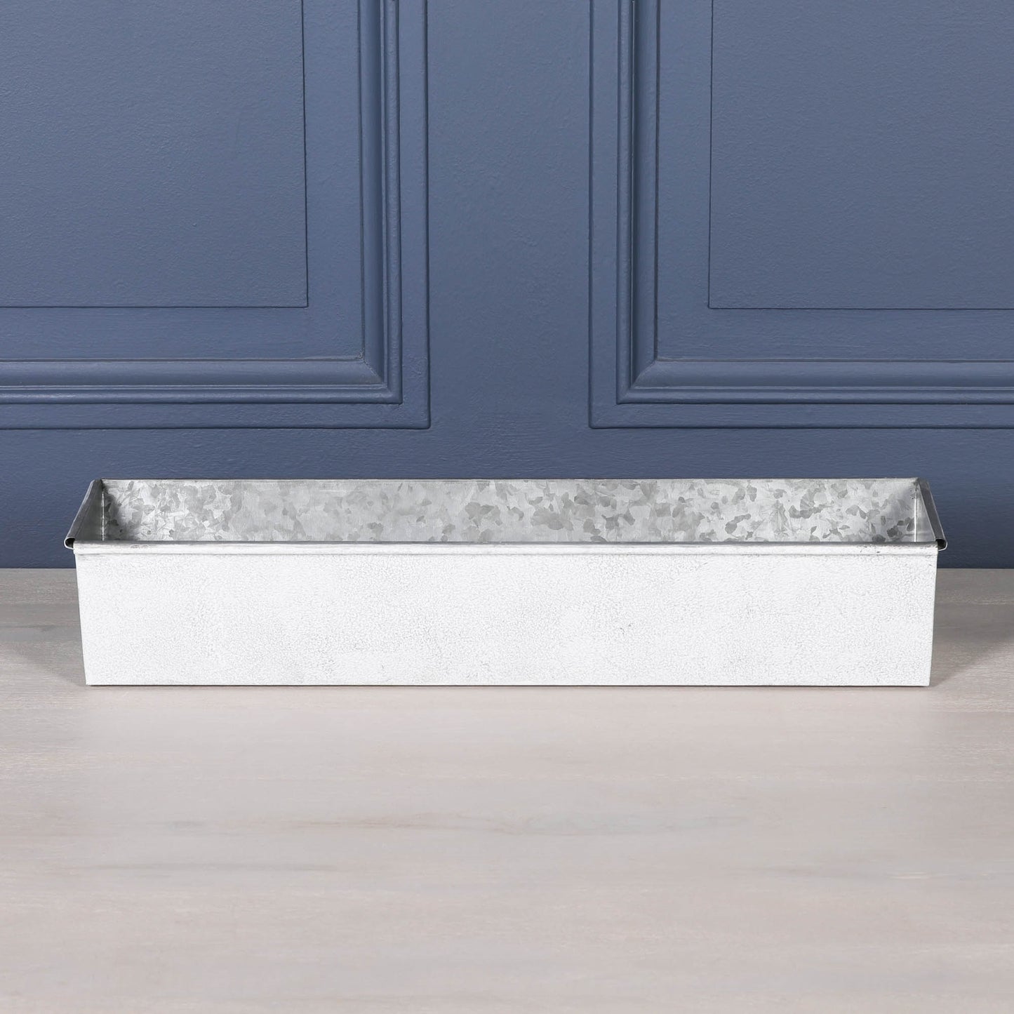 White wash metal window box planter with roll top design on a wooden surface.