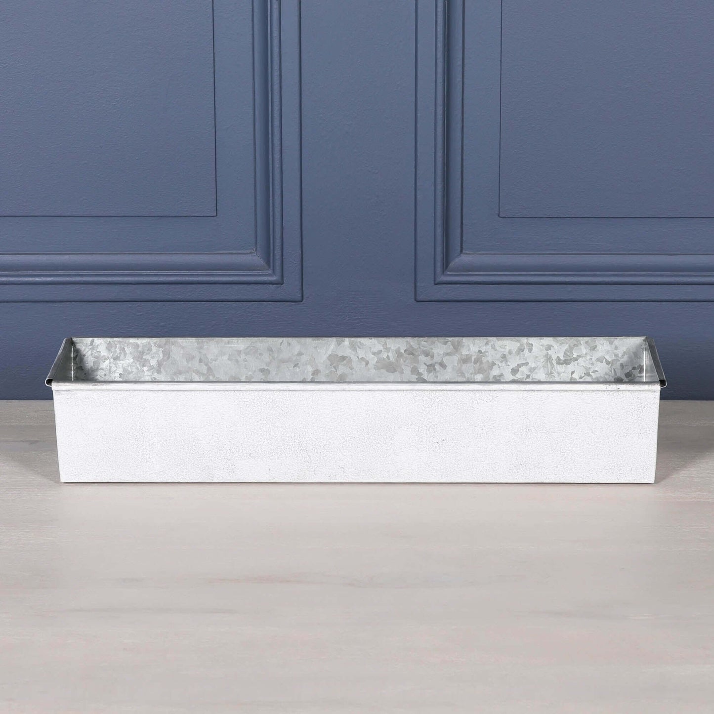 White wash metal window box planter with roll top design on a wooden surface.