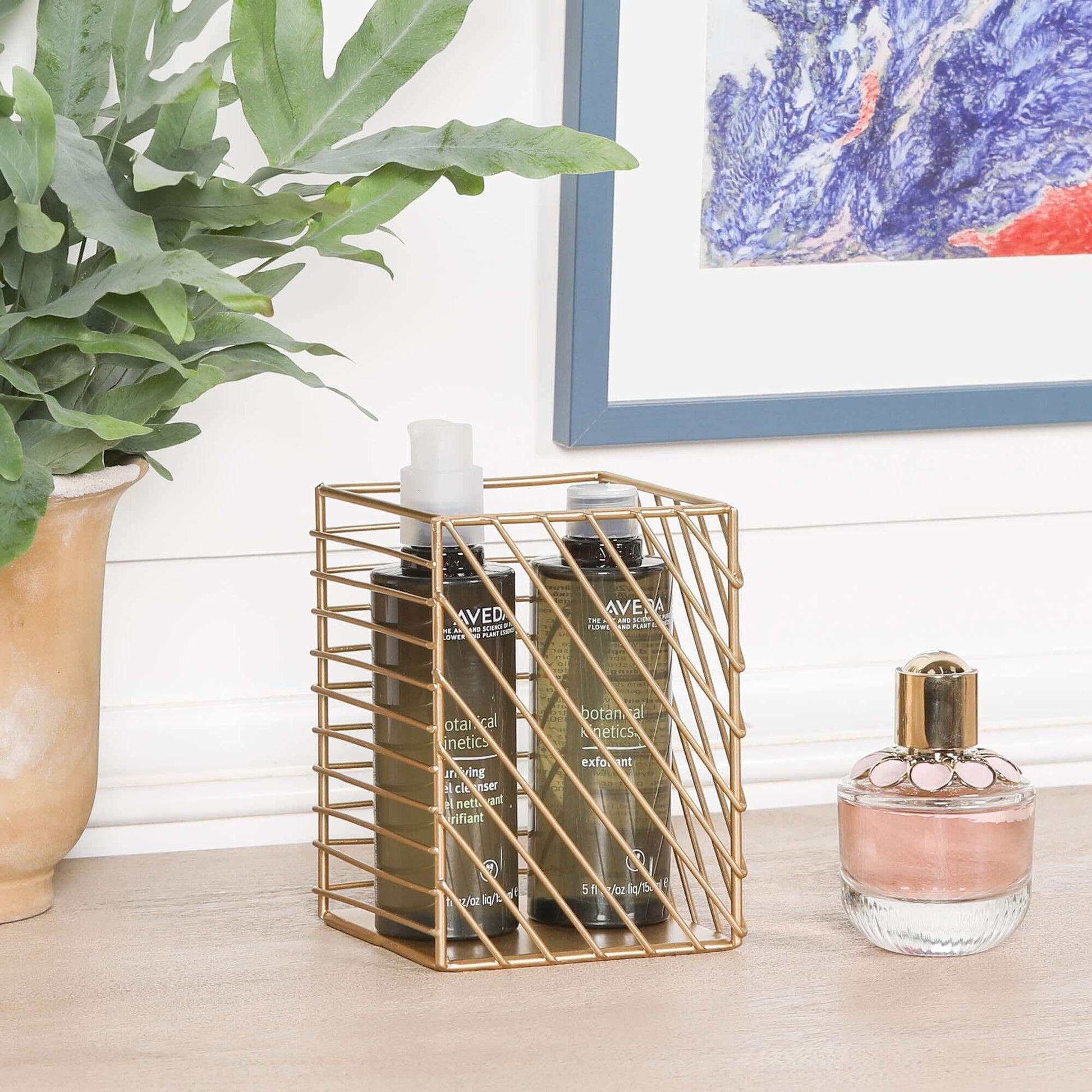 Gold Painted Square Metal Storage Basket holding beauty products on a wooden table with decorative plant.