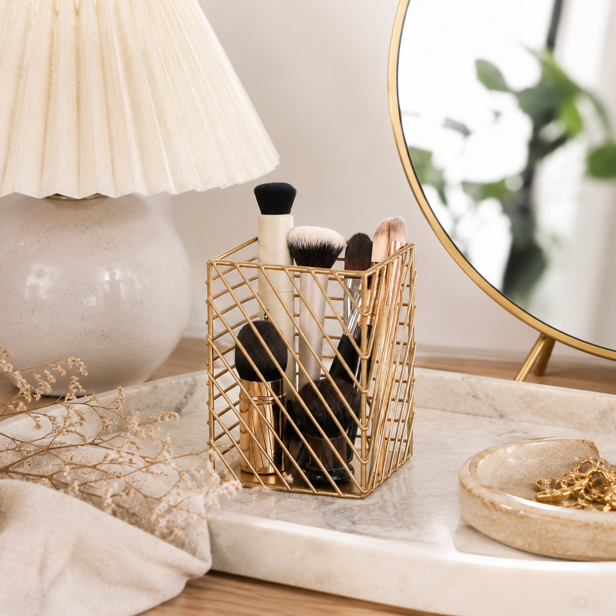 Gold Metal Storage Basket Organiser with makeup brushes on a marble tray with a marble jewellery holder and a cream lamp
