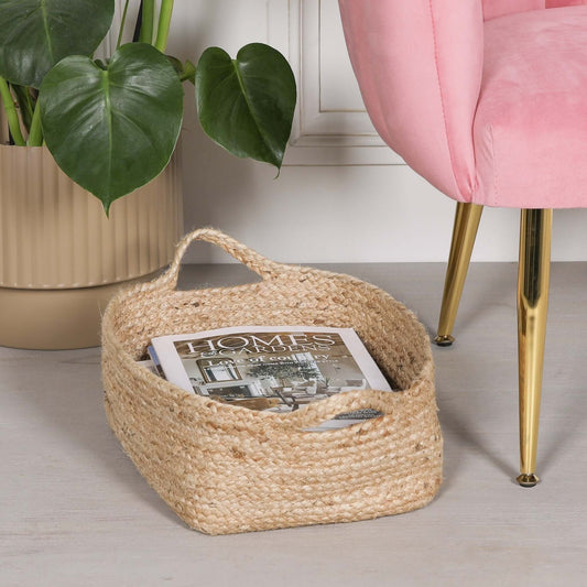 Jute Magazine Storage Basket holding a magazine, placed beside a pink chair and a potted plant.