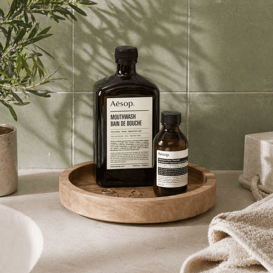 Two Aesop bottles on a wooden tray with a green tiled wall in the background