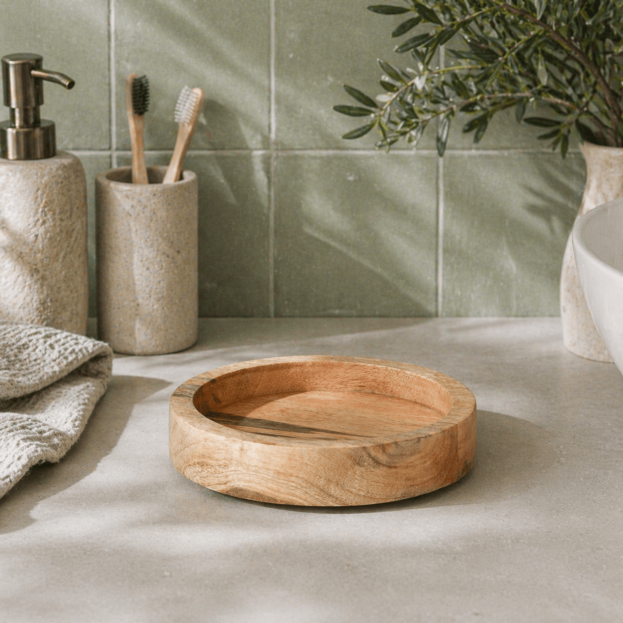 Bathroom setting with a wooden bowl, toothbrush holder, and soap dispenser on a tiled wall background.