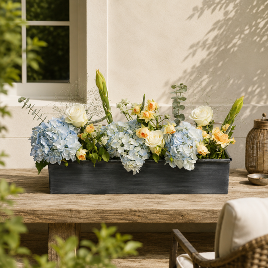 Floral arrangement in an iron planter on a wooden table outdoors.