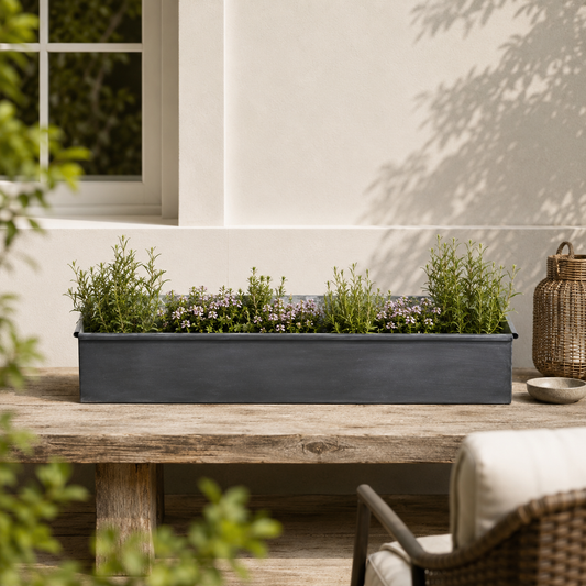 Long iron rectangular planter with green plants on a wooden table outdoors.