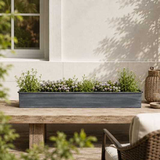 Long rectangular planter with greenery on a wooden table outdoors.