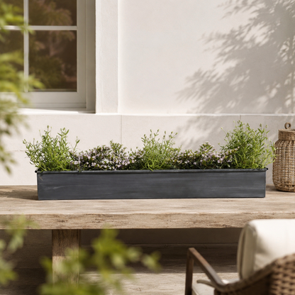Long iron rectangular planter with green plants on a wooden table outdoors.