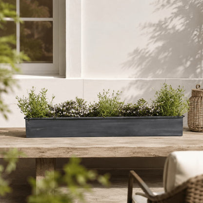 Iron weathered planter on wooden tabletop in a garden setting featuring herbs and flowers