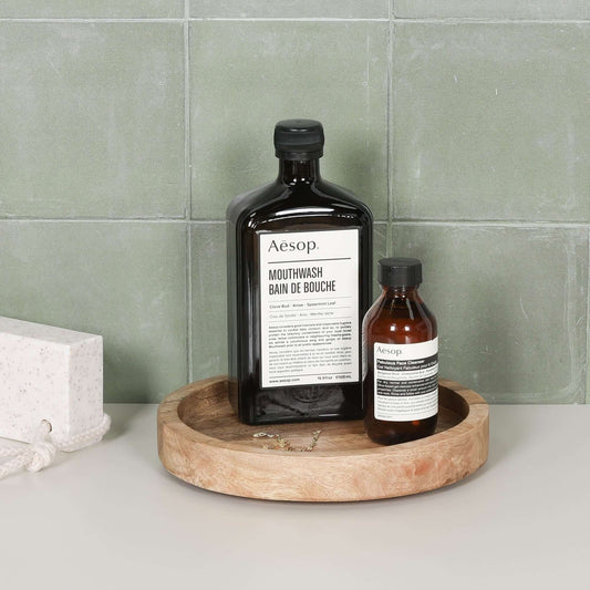 Round 20cm Wooden Tray holding Aesop mouthwash bottles on a stylish bathroom countertop.