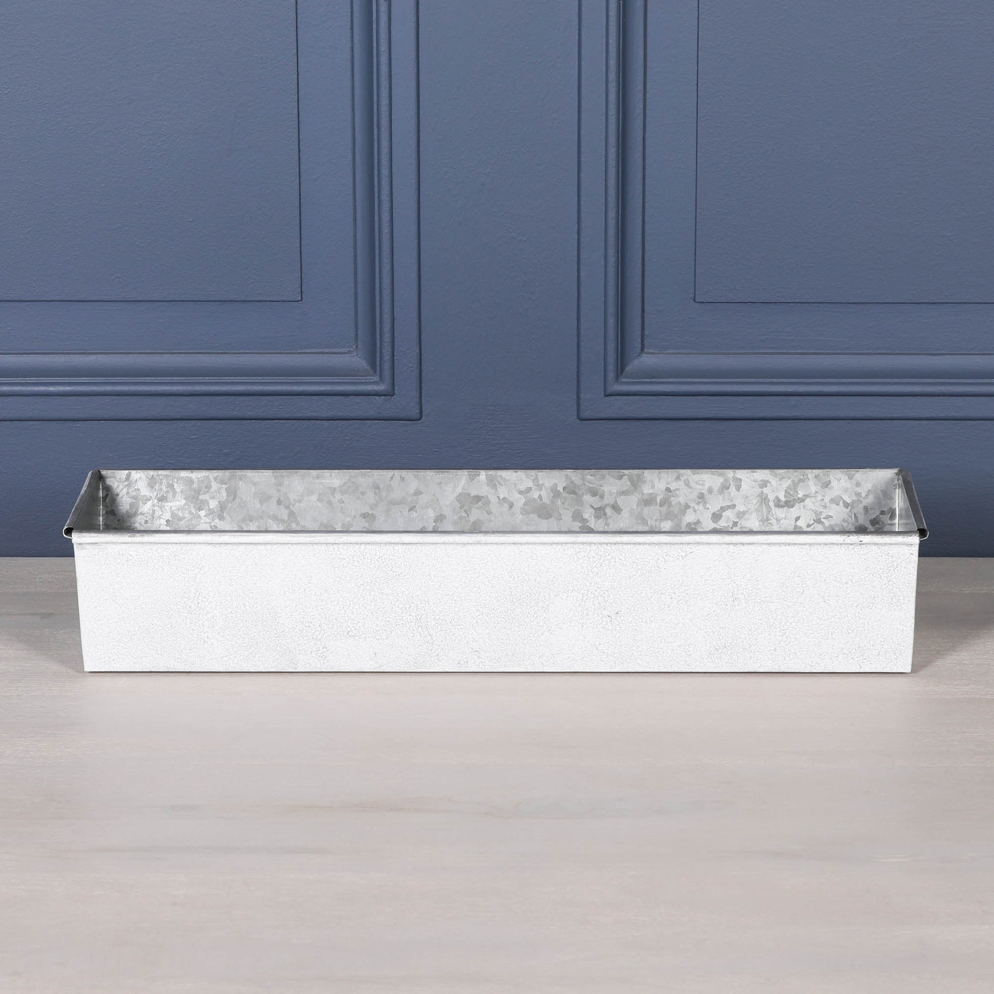 White wash metal window box planter with roll top design on a wooden surface.