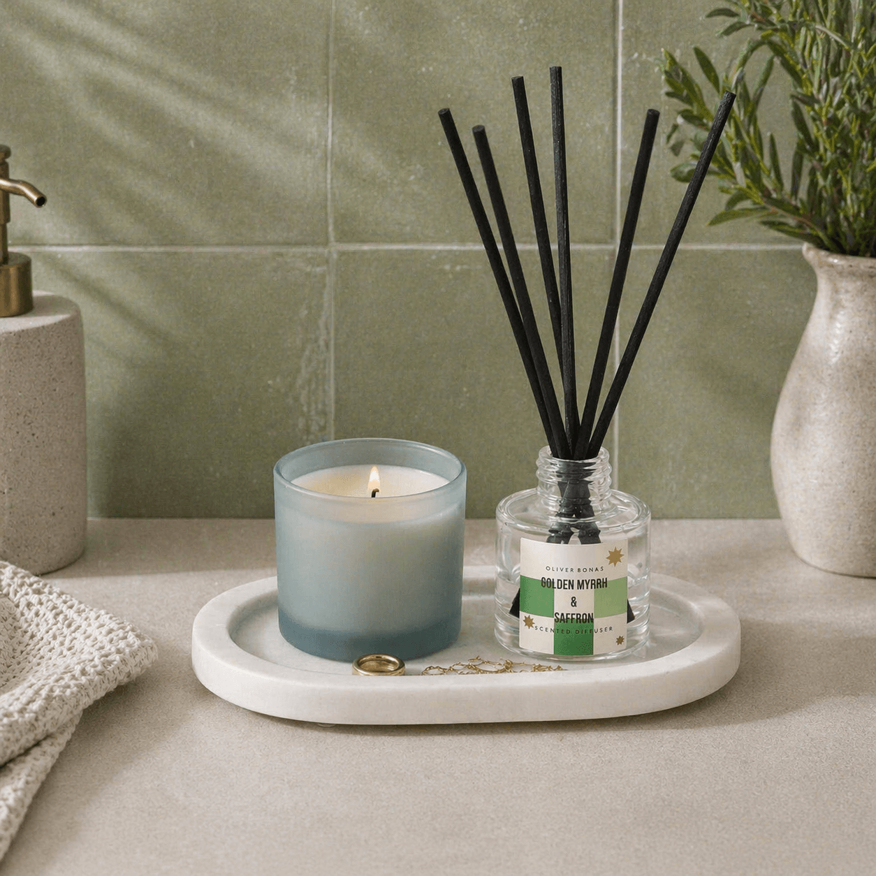 White marble decorative tray holding a candle, jewellery and a diffuser against green tiled wall