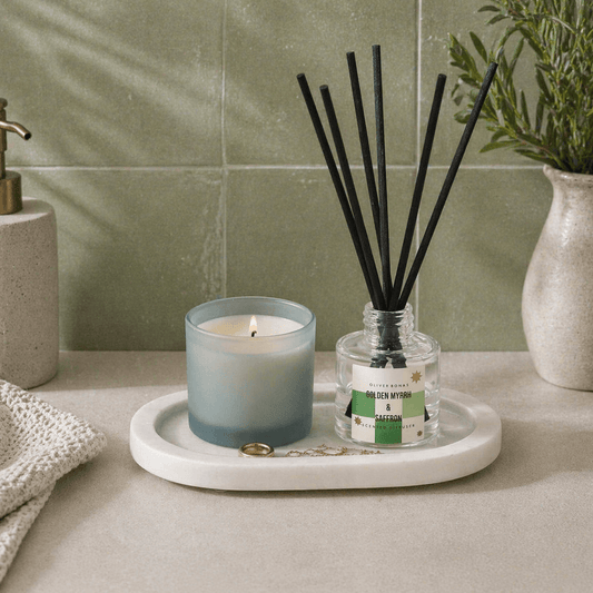 White marble decorative tray holding a candle, jewellery and a diffuser against green tiled wall