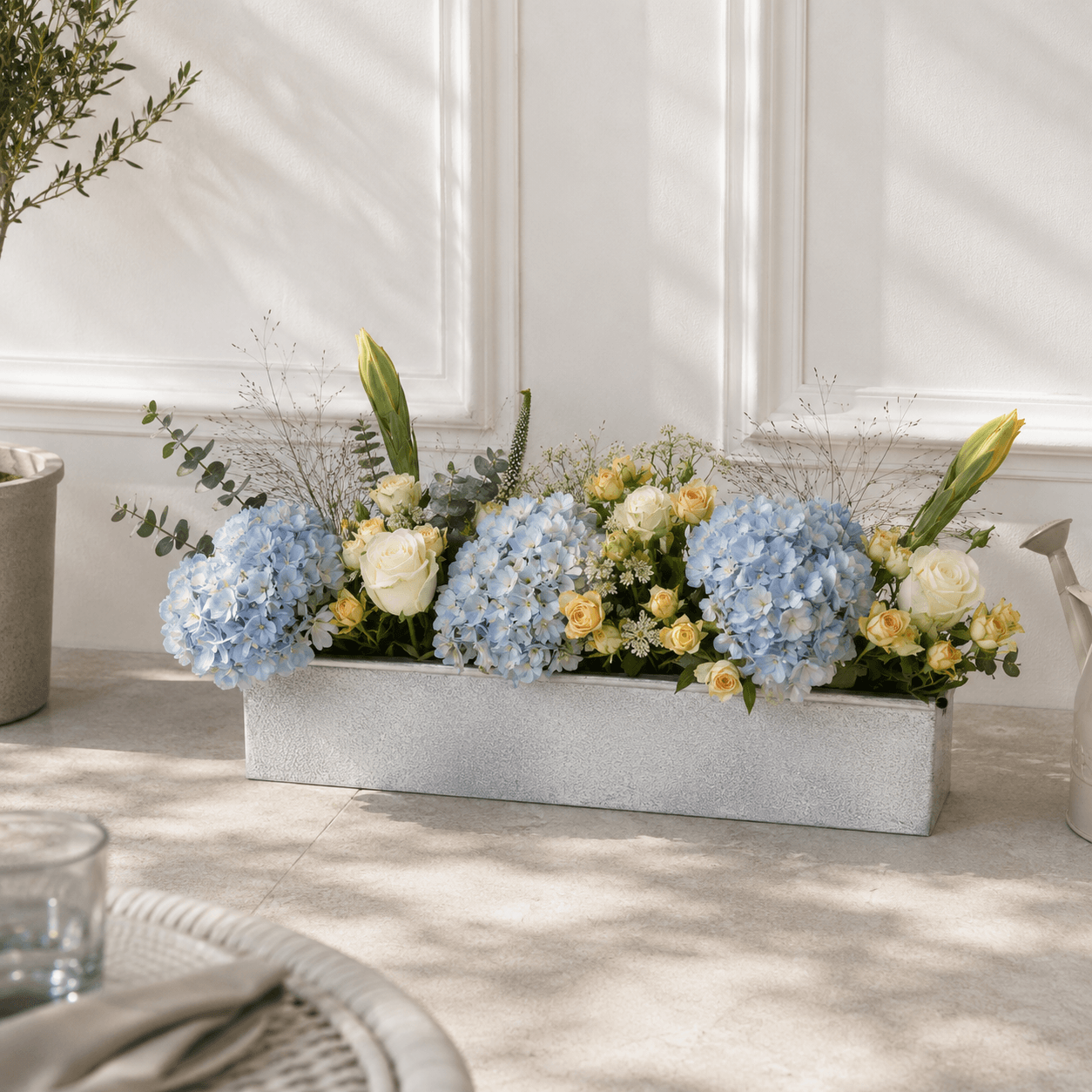 Metal planter in patio with blooms and flowers against white wall outdoors