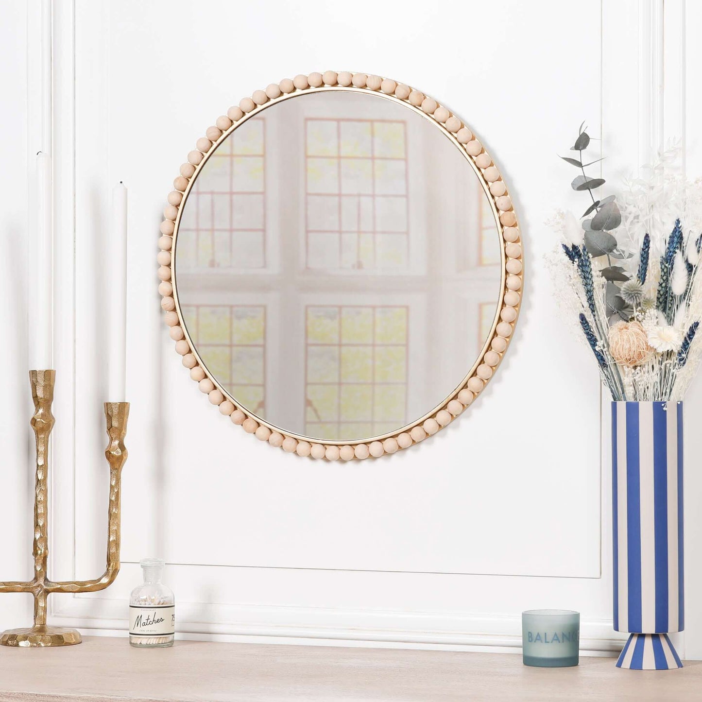 Wooden Bobble Round Wall Mirror displayed on a shelf with candles and flowers, showcasing its stylish design.